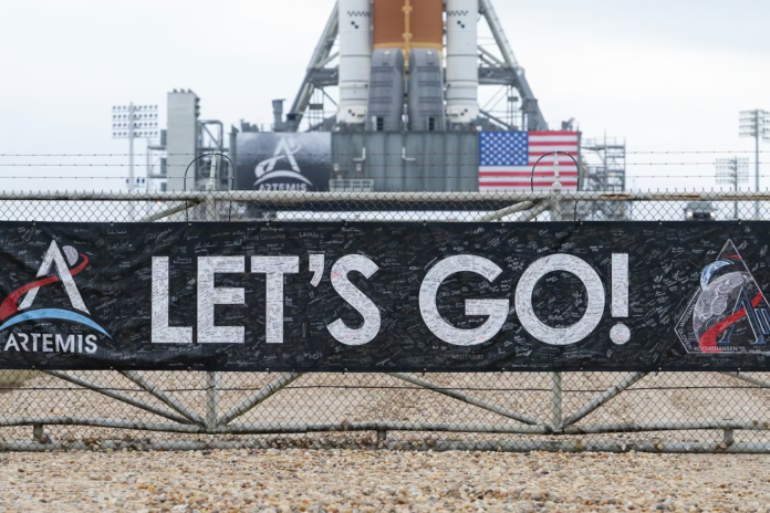 A banner signed by NASA employees and contractors outside Launch Complex 39B, where NASA’s Artemis II rocket is visible in the background. NASA/Joel Kowsky, CC BY-NC-ND